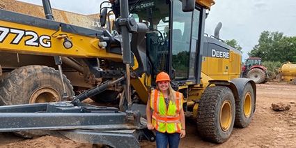 An engineering intern in a safety vest and hard hat standing in front of equipment.