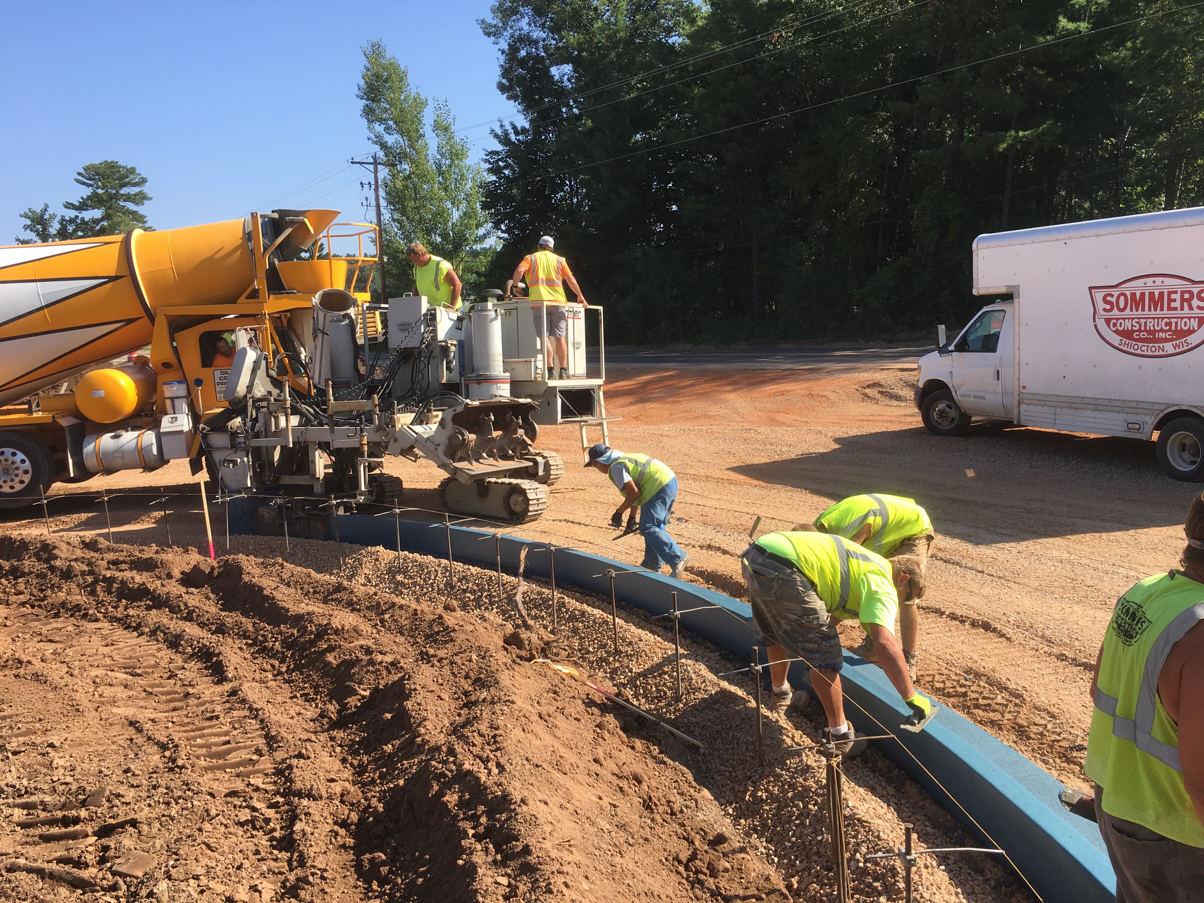 A yellow and white cement truck and construction workers working on blue concrete.