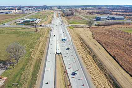 State highway viewed from above, two lanes are closed to traffic with orange barrels.