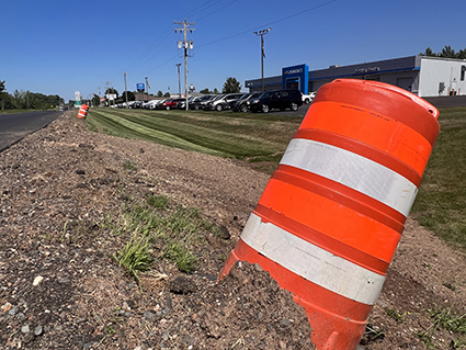 Orange barrels line the road near a car dealership.