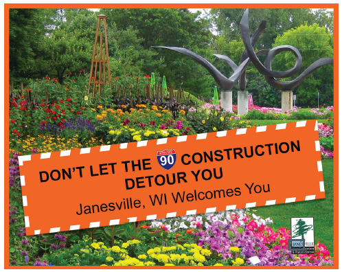 Large flower garden with a orange sign "DON'T LET THE I-90 CONSTRUCTION DETOUR YOU.  Janesville, WI Welcomes You."